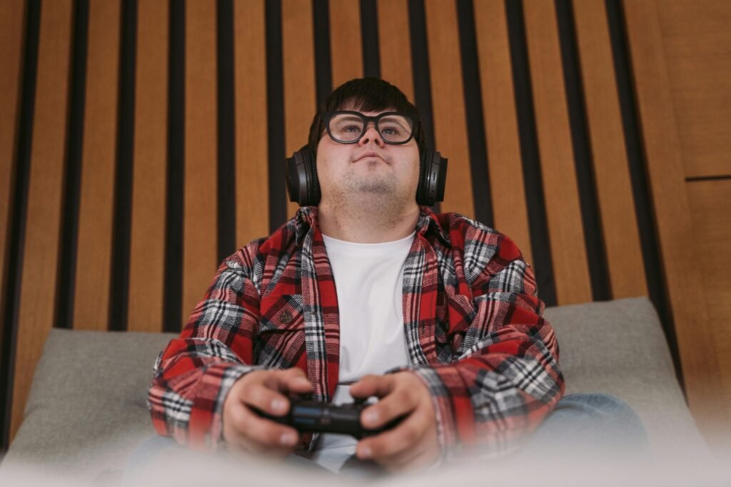 Young man wearing headphones and plaid shirt playing video games indoors.