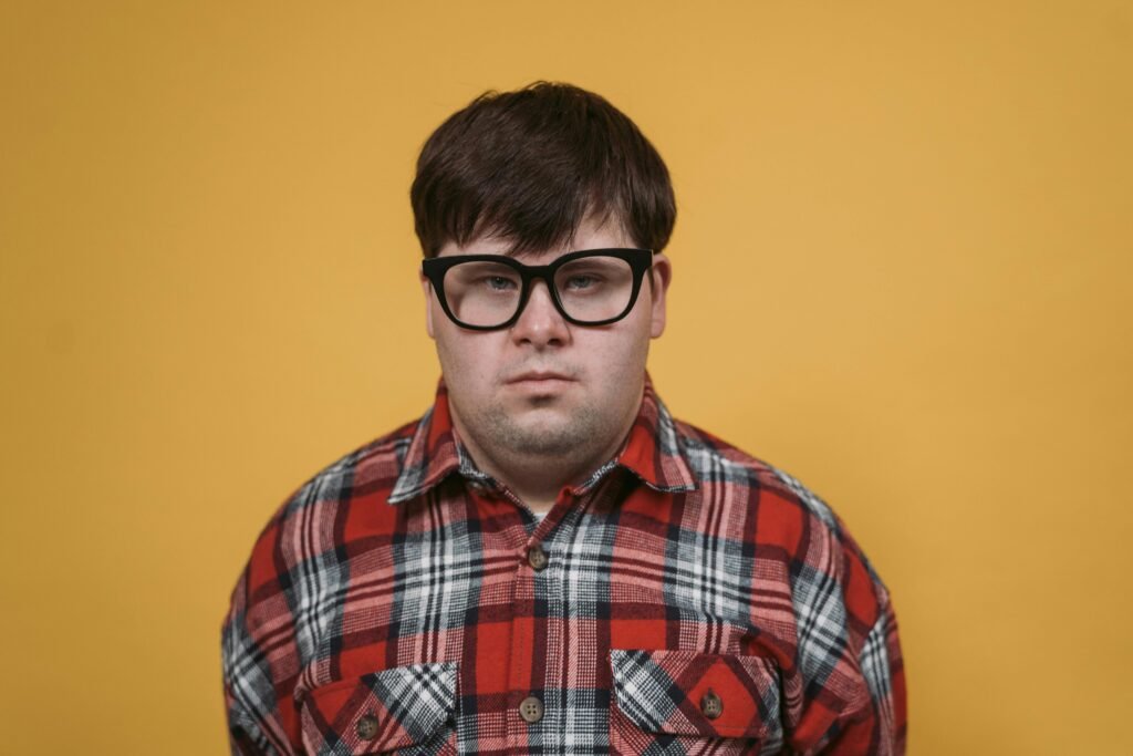 Close-up studio portrait of a man wearing eyeglasses and a plaid shirt on a yellow background.
